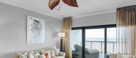 A modern living room with a sofa, a coffee table, a painting, and a view of the sea through large windows.