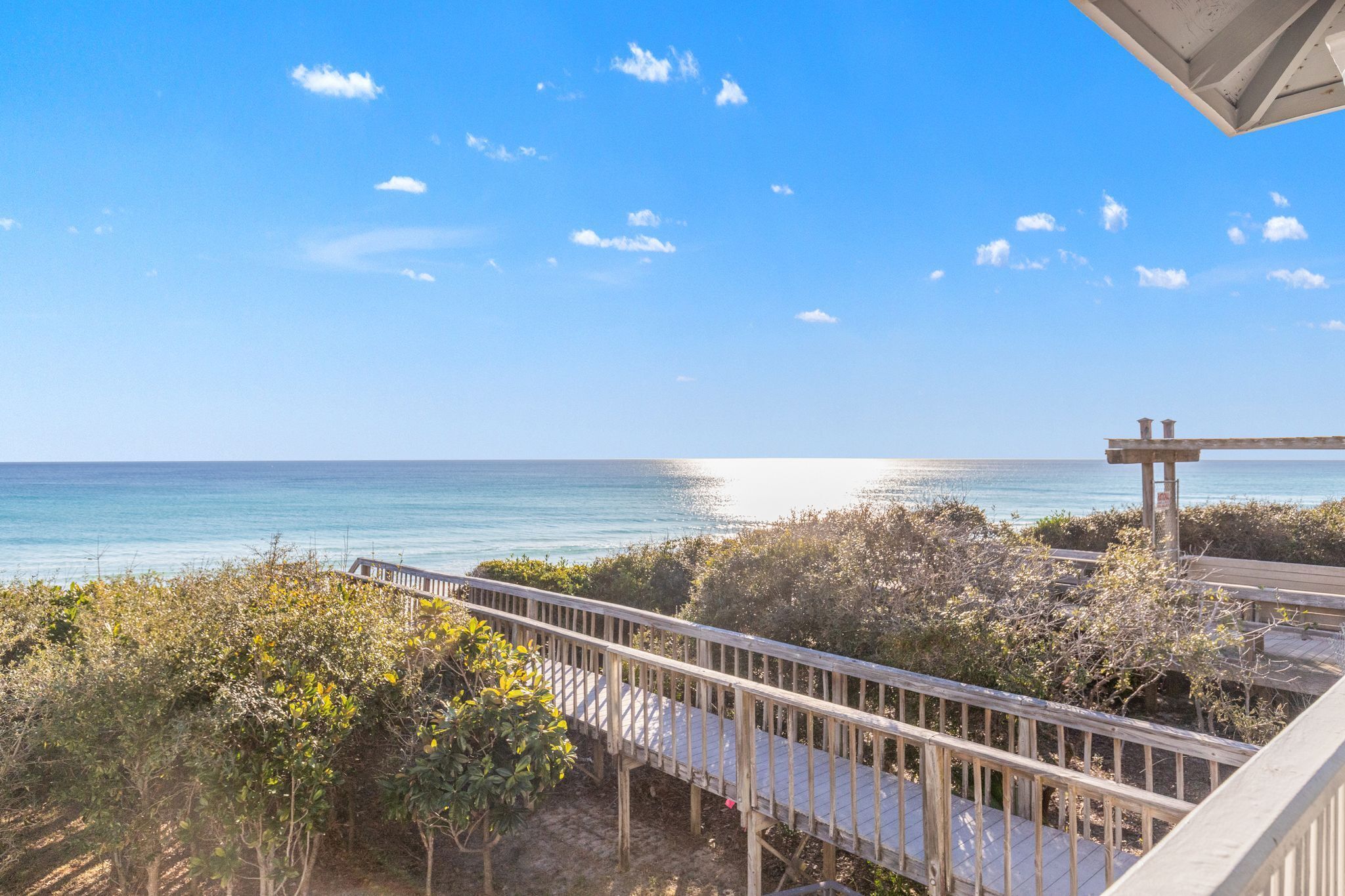 A wooden boardwalk leading to a beach with clear blue water and a few clouds in the sky.