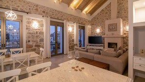 Una sala de estar acogedora con pared de piedra, chimenea, televisor y comedor con mesa y sillas.