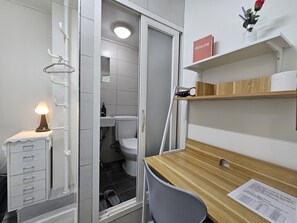 A compact bathroom with a toilet, sink, and a mirror. There is a wooden desk with a chair, a small shelf with a book, and a lit lamp. - Only for woman - Sadang House (Seoul)