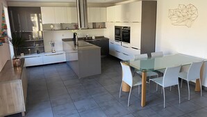 A modern kitchen with white cabinets, stainless steel appliances, and a glass dining table with white chairs.