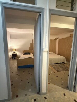 A hotel room with two beds, a nightstand, a lamp, and a patterned carpet. - On the road to the rivers and the Carbet peaks. Quiet, leafy neighborhood. (Fort-de-France)