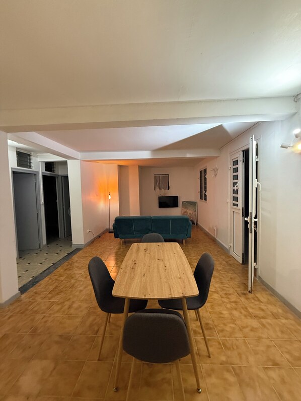A room with a wooden table, four chairs, a teal sofa, a TV, and a door.