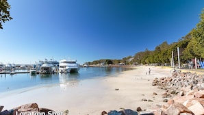 A marina with boats docked, a sandy beach with rocks, and a playground. - A Yachtsman Rest, 3-37 Victoria Pde - stunning unit with stunning views (Nelson Bay)