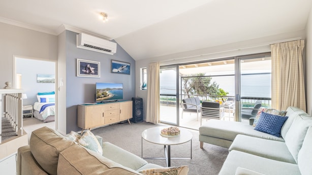 A modern living room with a sofa, a coffee table, and a TV. There is a balcony with a view of the sea. - A Yachtsman Rest, 3-37 Victoria Pde - stunning unit with stunning views (Nelson Bay)