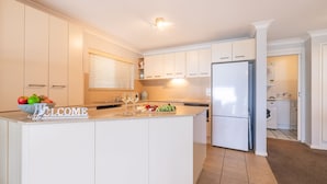 A modern kitchen with a central island, white cabinetry, and a built-in washing machine. - A Yachtsman Rest, 3-37 Victoria Pde - stunning unit with stunning views (Nelson Bay)
