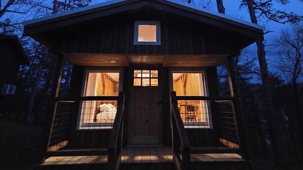 A wooden cabin with a central door, two windows on either side, and a small porch with steps leading up to the entrance. - Lazy T Cabins - Grand Teton (Graham County)