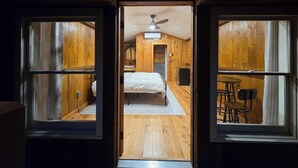 Eine Holzhütte mit einem Schlafzimmer, das ein Bett, einen Deckenventilator und einen kleinen Tisch mit Stühlen bietet.