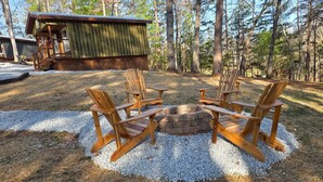 Eine Holzterrasse mit Adirondack-Stühlen und einem Feuerkorb aus Stein, umgeben von Kies.