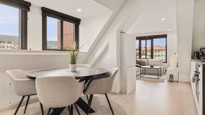 Ein modernes Interieur mit einem runden Esstisch, vier Stühlen, einer Topfpflanze und Blick ins Freie durch große Fenster.