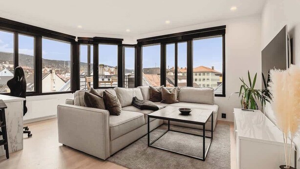 Ein modernes Wohnzimmer mit Ecksofa, Couchtisch und großen Fenstern mit Blick auf die Stadt.