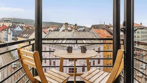 Ein Balkon mit einem Holztisch und Stühlen, mit Blick auf eine Stadtlandschaft mit Gebäuden und einer Straße.