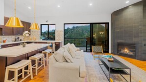 Un salon moderne avec un canapé, une table basse et une cheminée. Il y a également un coin cuisine avec un grand îlot central et des luminaires suspendus.