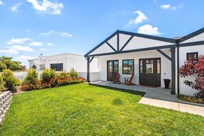 Ein modernes Haus mit überdachter Veranda, gepflegtem Rasen und einem kleinen Garten mit roten Blüten.