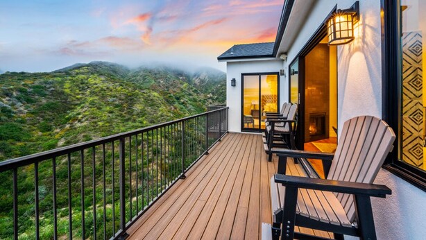 Un balcon offrant une vue sur un paysage montagneux, une cheminée et deux fauteuils Adirondack.