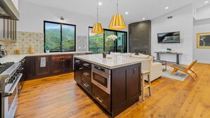 Une cuisine moderne dotée d’un grand îlot central, de planchers en bois et de luminaires suspendus.