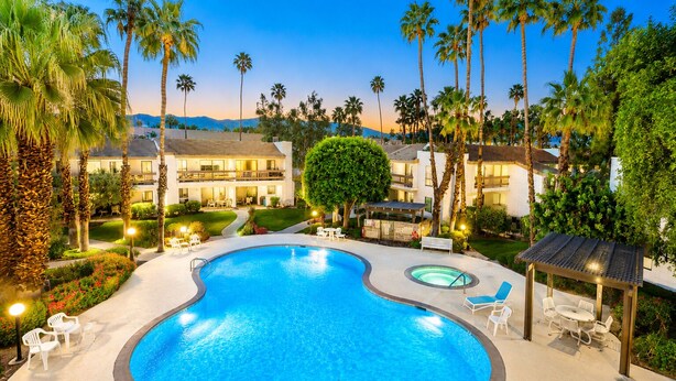 A swimming pool with lounge chairs, surrounded by palm trees and a building with multiple balconies. - Beautiful Community! Pool, Jacuzzi, Tennis, Golf (Palm Springs)