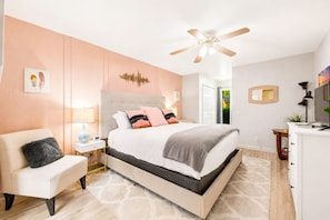 A bedroom with a bed, a chair, a desk, a ceiling fan, and a door leading to a balcony.