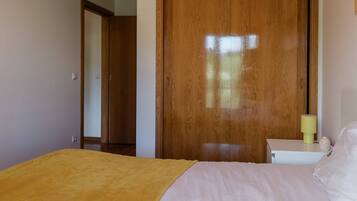 A bedroom with a bed, a wooden wardrobe, and a nightstand with a lamp.