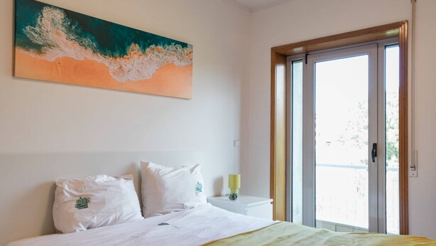 A bedroom with a bed, a painting, a window, and a door. - Gaia Beach&Golf – EcoHost | Parking · Surf · 5 pax (Arcozelo)