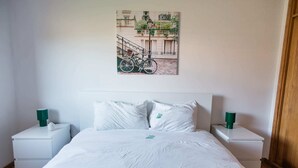 A bedroom with a bed, white nightstands, and a wall-mounted picture. - Gaia Beach&Golf – EcoHost | Parking · Surf · 5 pax (Arcozelo)