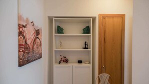 A room with a white cabinet, a wooden door, and a macrame chair. - Gaia Beach&Golf – EcoHost | Parking · Surf · 5 pax (Arcozelo)