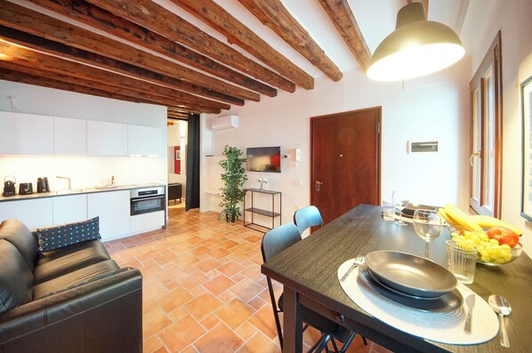 A modern kitchen with white cabinets, a dining table set with plates, glasses, and a fruit bowl.
