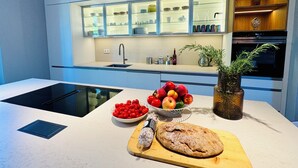 Una cocina moderna con horno empotrado, un lavamanos y una encimera con tabla de cortar, un cuenco de fruta y una hogaza de pan.