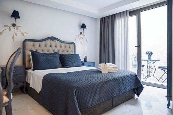 A bedroom with a large bed, two bedside tables, a chair, a nightstand, a window with curtains, and a balcony with a table and chairs. - Voger Alaçatı Family (Cesme)