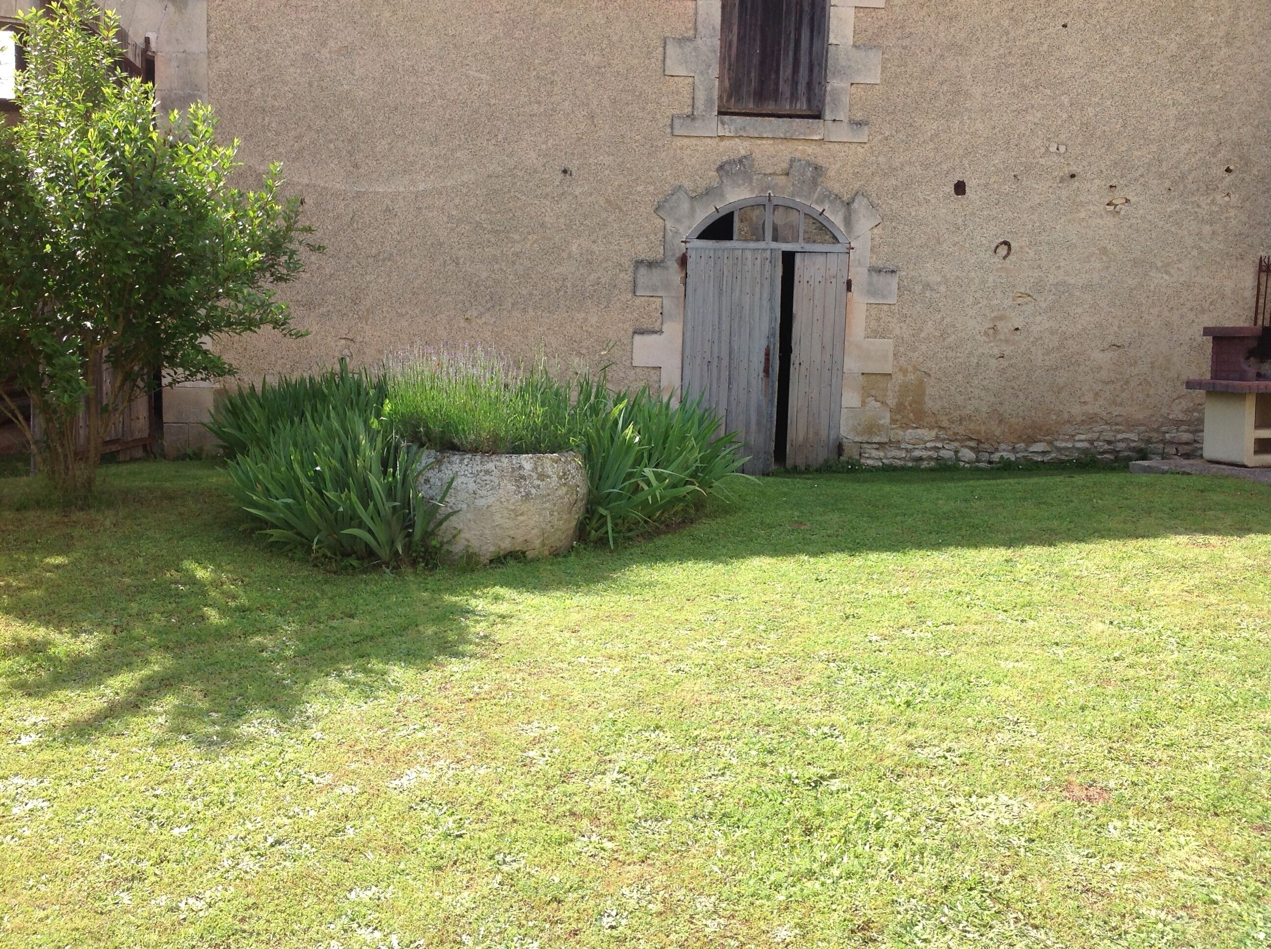 Ein Gebäude mit einer Steinfassade, einer Holztür und einem kleinen Garten mit Gras und Pflanzen.