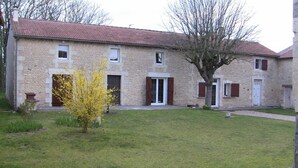A stone building with a tiled roof, a small garden, and a tree with yellow flowers.