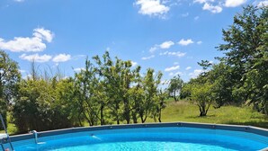 A round above-ground swimming pool with a tiled interior, surrounded by grass and trees.