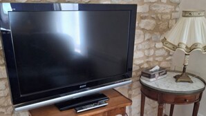 A flat-screen TV on a wooden stand, a small table with a lamp, and a stone wall.