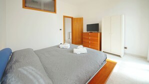 Ein Schlafzimmer mit einem Bett, einem Kleiderschrank, einem Fernseher und einer Tür zu einem anderen Raum.