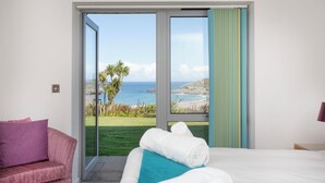 Une chambre dotée d’une grande porte-fenêtre coulissante donnant sur un balcon avec vue sur la mer et un espace verdoyant.