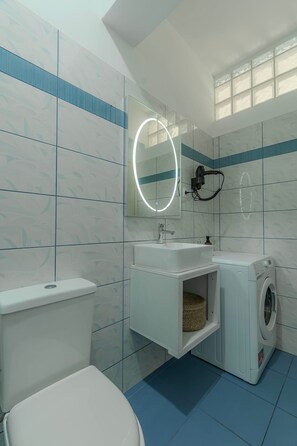 Een moderne badkamer met toilet, wastafel, spiegel en wasmachine.