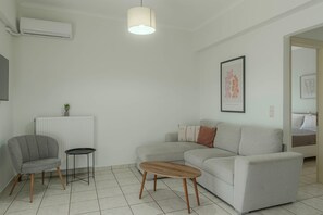 A modern living room with a grey sofa, a small round table, a radiator, and a ceiling light fixture.