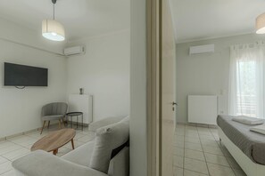 Een moderne woonkamer met een flatscreen televisie, een grijze bank, een klein rond tafeltje en een radiator.