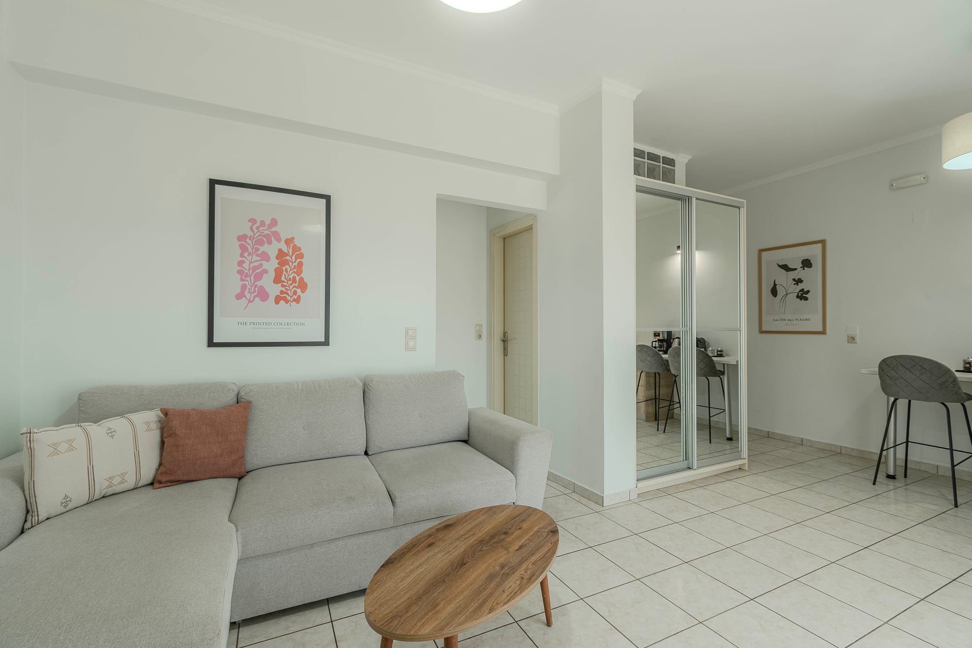 A modern living room with a grey sofa, a round wooden coffee table, and a dining area with a high chair.