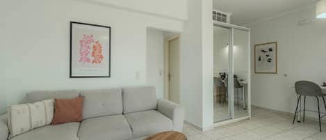 Una sala moderna con un sofá gris, una mesa de centro redonda de madera y un comedor con una silla alta.