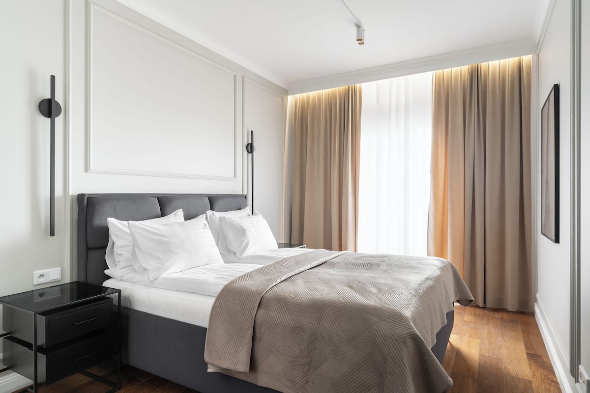 Ein modernes Schlafzimmer mit einem Bett, Nachttischen und einem großen Fenster mit Vorhängen.