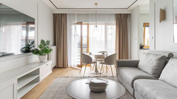 A modern living room with a sofa, a dining table with chairs, a potted plant, and a large window with curtains. - Riverside Nadmotławie - Sauna, Gym & Kids Play by Lion Apartments (Gdansk)
