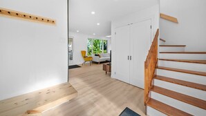 A modern interior with a wooden staircase, a yellow chair, and a white sofa in a bright room with wooden flooring and white walls.