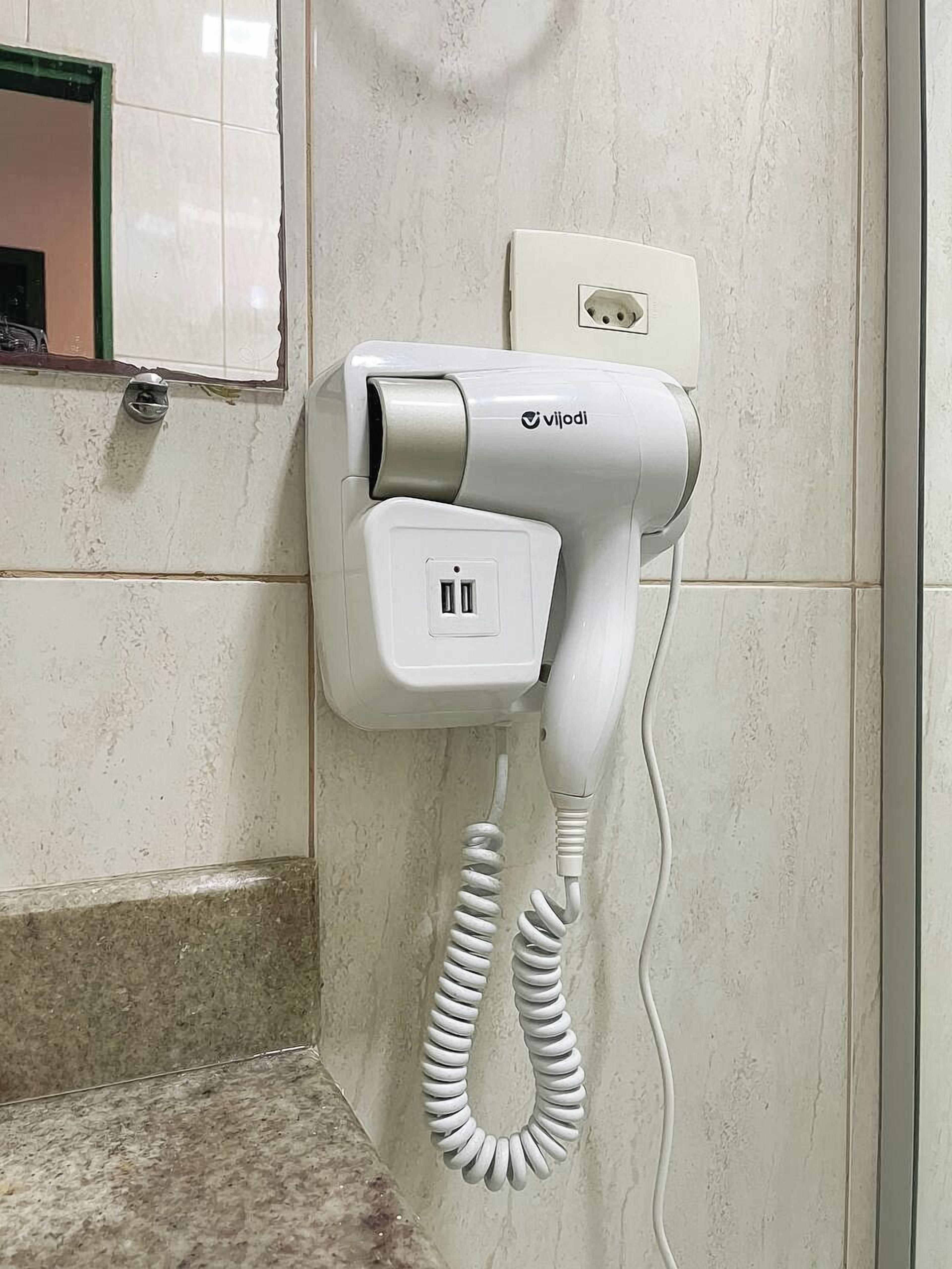 Un sèche-cheveux fixé au mur, muni d’un cordon, d’une prise de courant et d’un miroir avec un cadre vert.