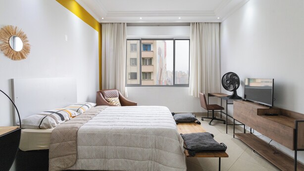 Een moderne hotelkamer met een groot bed, een bureau met een computer, een televisie en uitzicht op de stad.