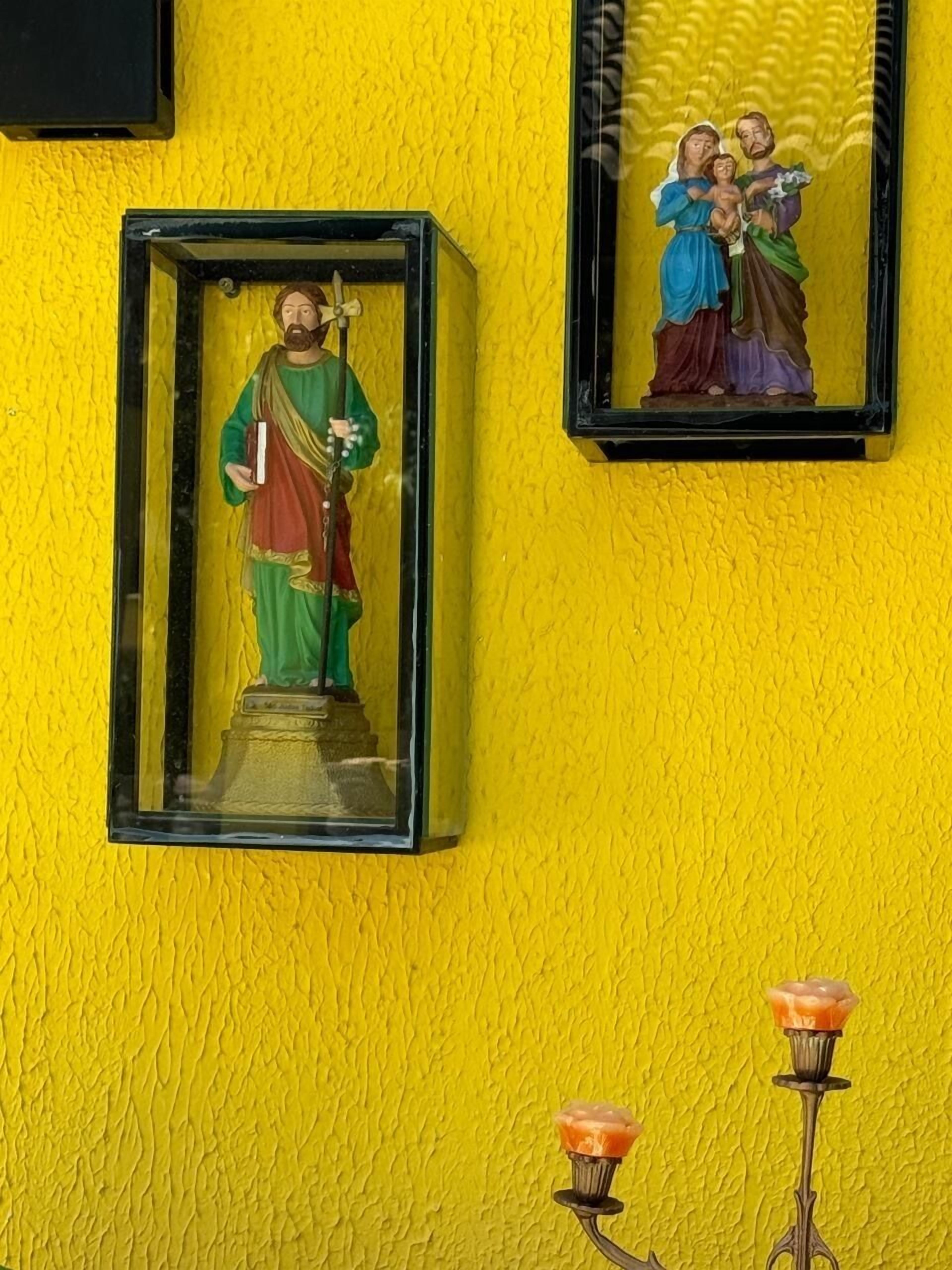 A statue of a religious figure in a glass case on a yellow wall.