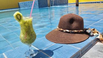Uma área de piscina com uma bebida num copo e um canudo, e um chapéu de palha na borda da piscina.