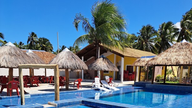 Une piscine dont les bords sont recouverts de carreaux, avec des chaises longues et des parasols en chaume.