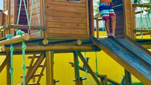 Une cabane en bois avec un toboggan, une échelle et une fenêtre.