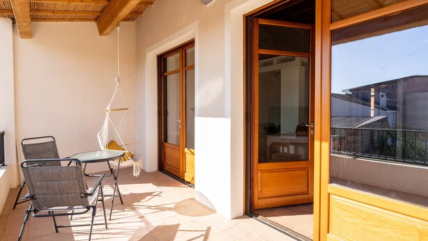 A balcony with a table and chairs, wooden doors, and a view of buildings. - Casa Tharros in Nurachi (Nurachi)